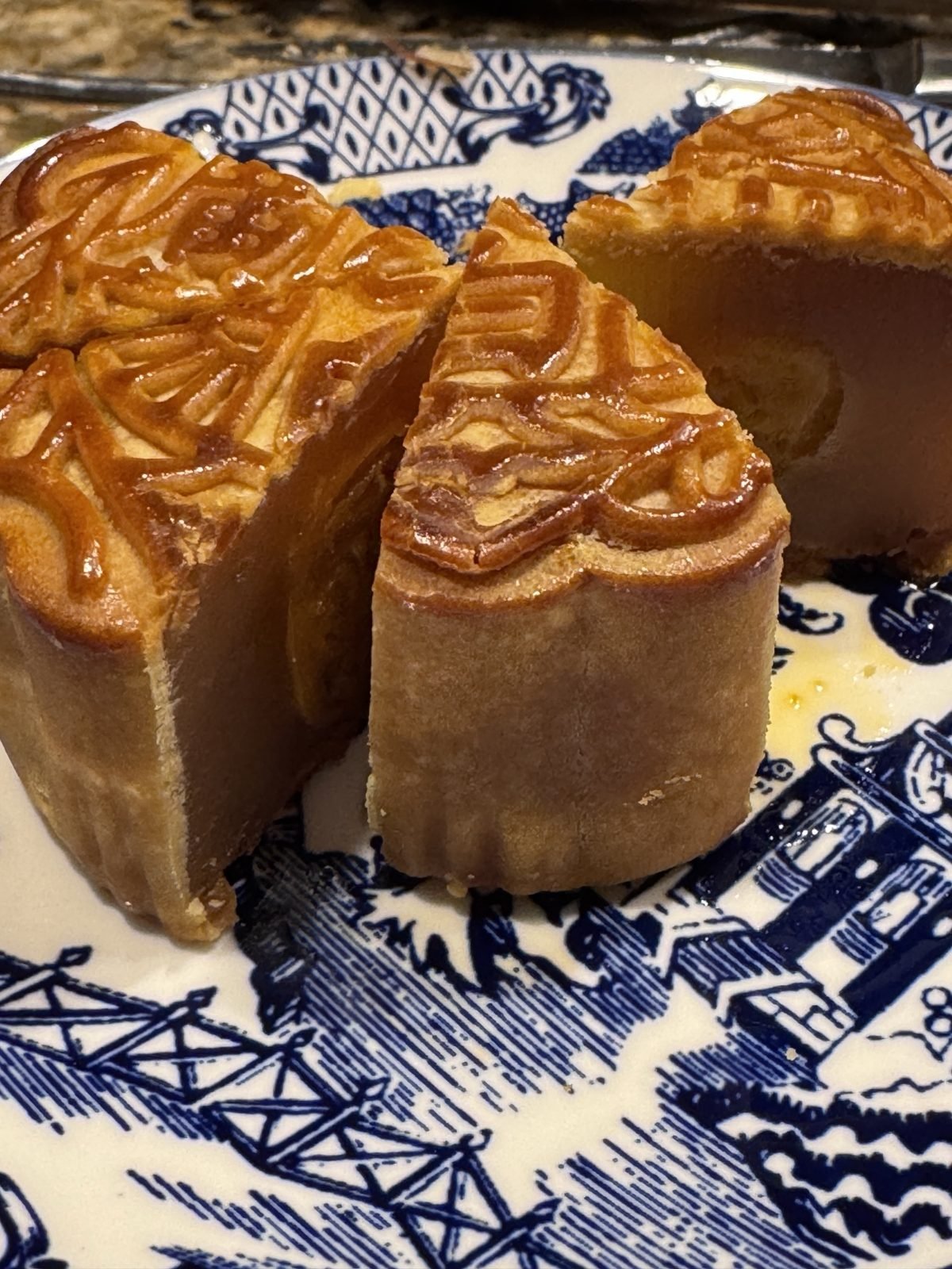 A moon cake cut into wedges on a blue and white willow-pattern plate